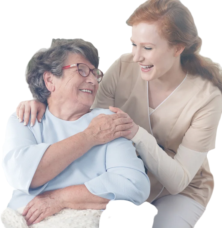 A carer in a soft beige uniform hugging a smiling elderly woman in a wheelchair